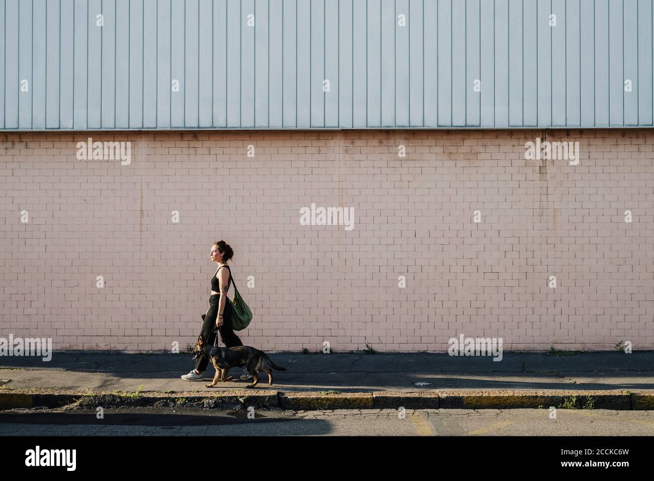 Woman walking with dog at sidewalk against wall Stock Photo