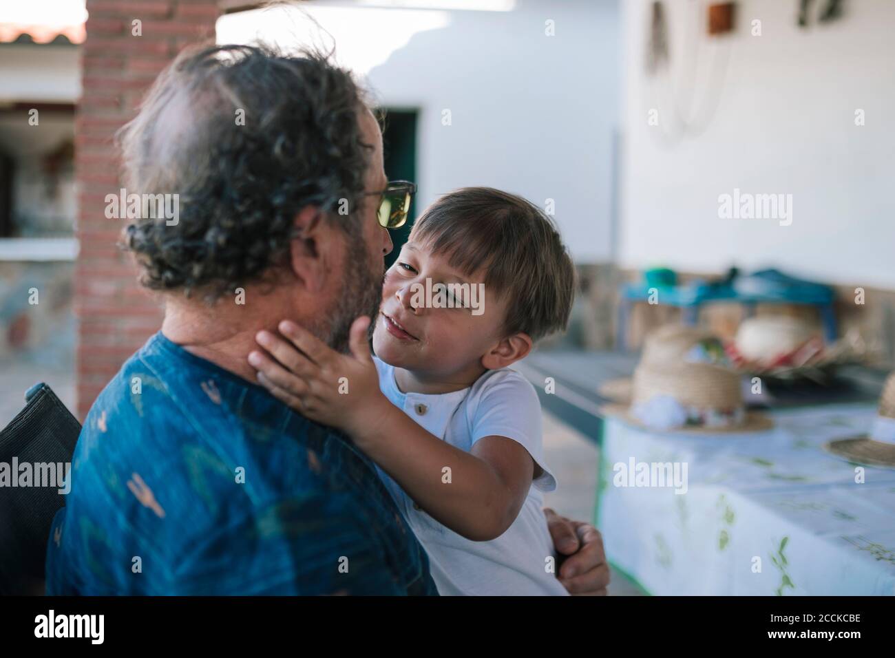 Grandchild holding grandfather's face affectionately while sitting outside house Stock Photo