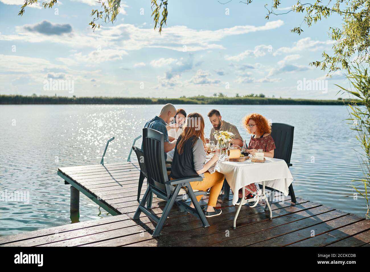 Friends having dinner on jetty at a lake Stock Photo