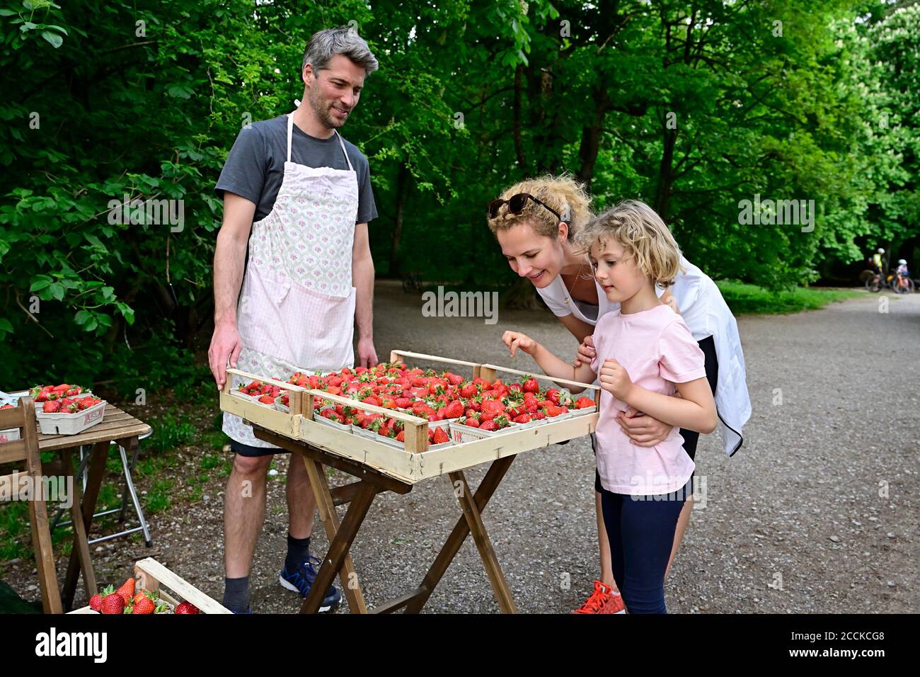 Male vendor looking at woman with daughter choosing strawberries at market stall Stock Photo