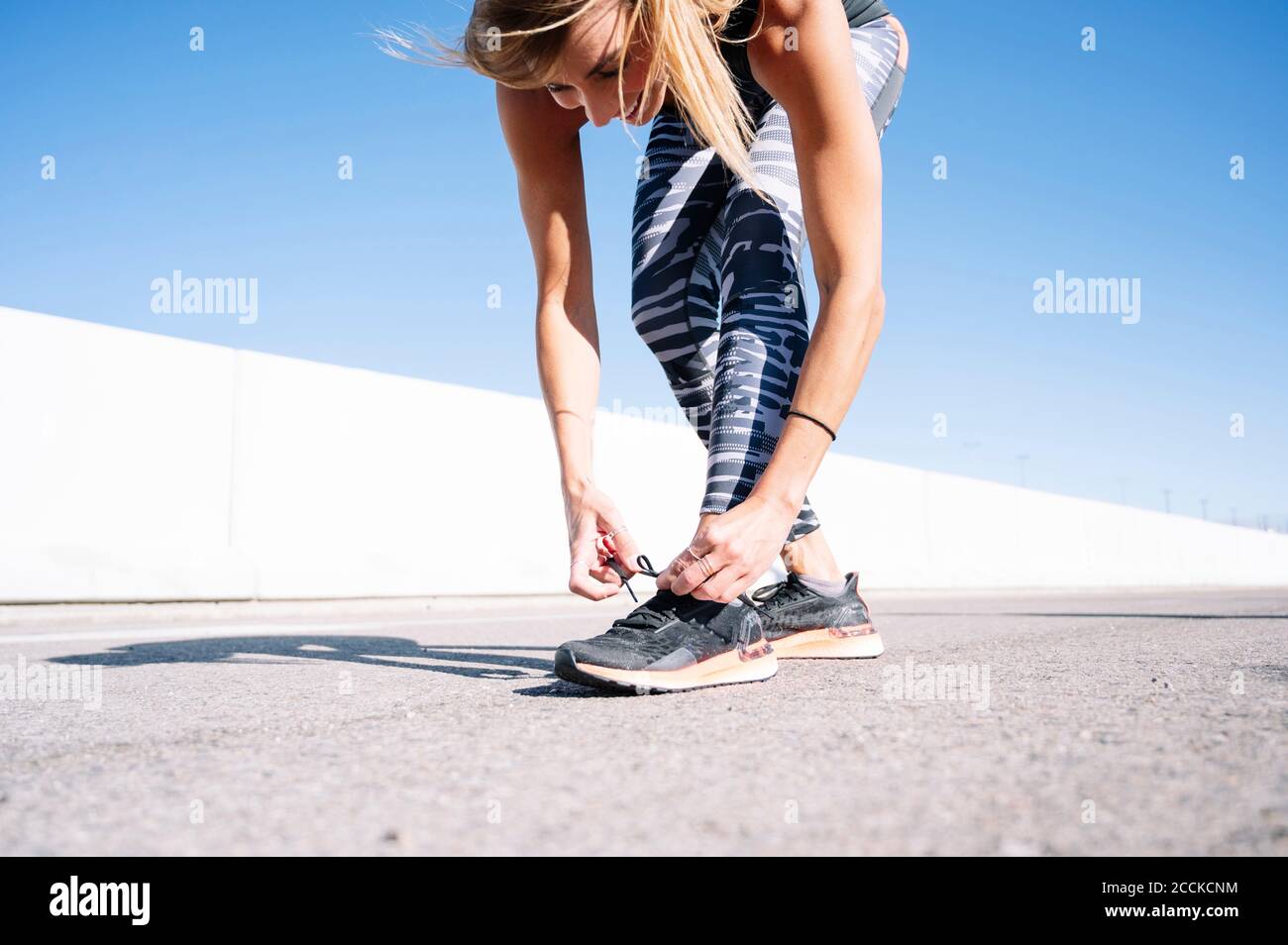Mid adult woman tying shoelace on road against clear blue sky in city Stock Photo