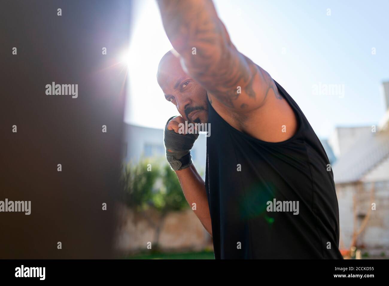Confident mature man practicing boxing with punching bag against clear sky in yard Stock Photo