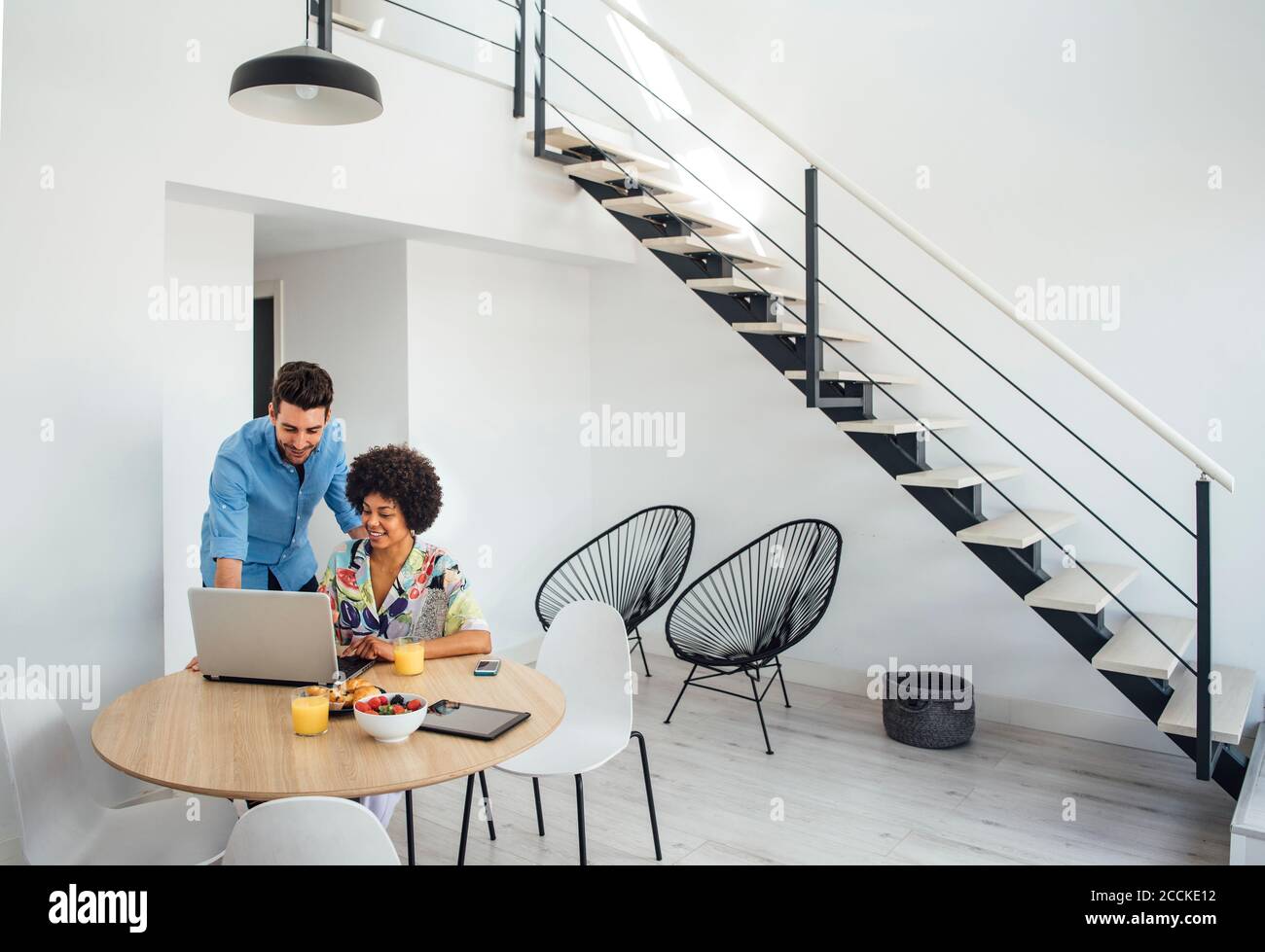 Multi-ethnic couple using laptop at dining table in modern penthouse Stock Photo