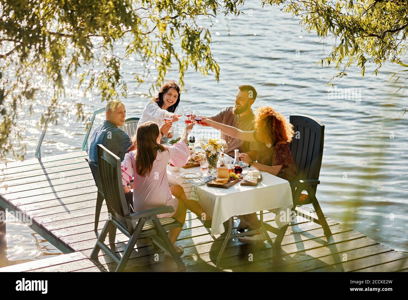 Friends having dinner on jetty at a lake clinking wine glasses Stock Photo