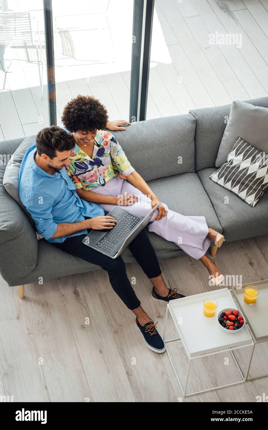 Multi-ethnic couple using laptop while sitting on sofa in penthouse Stock Photo