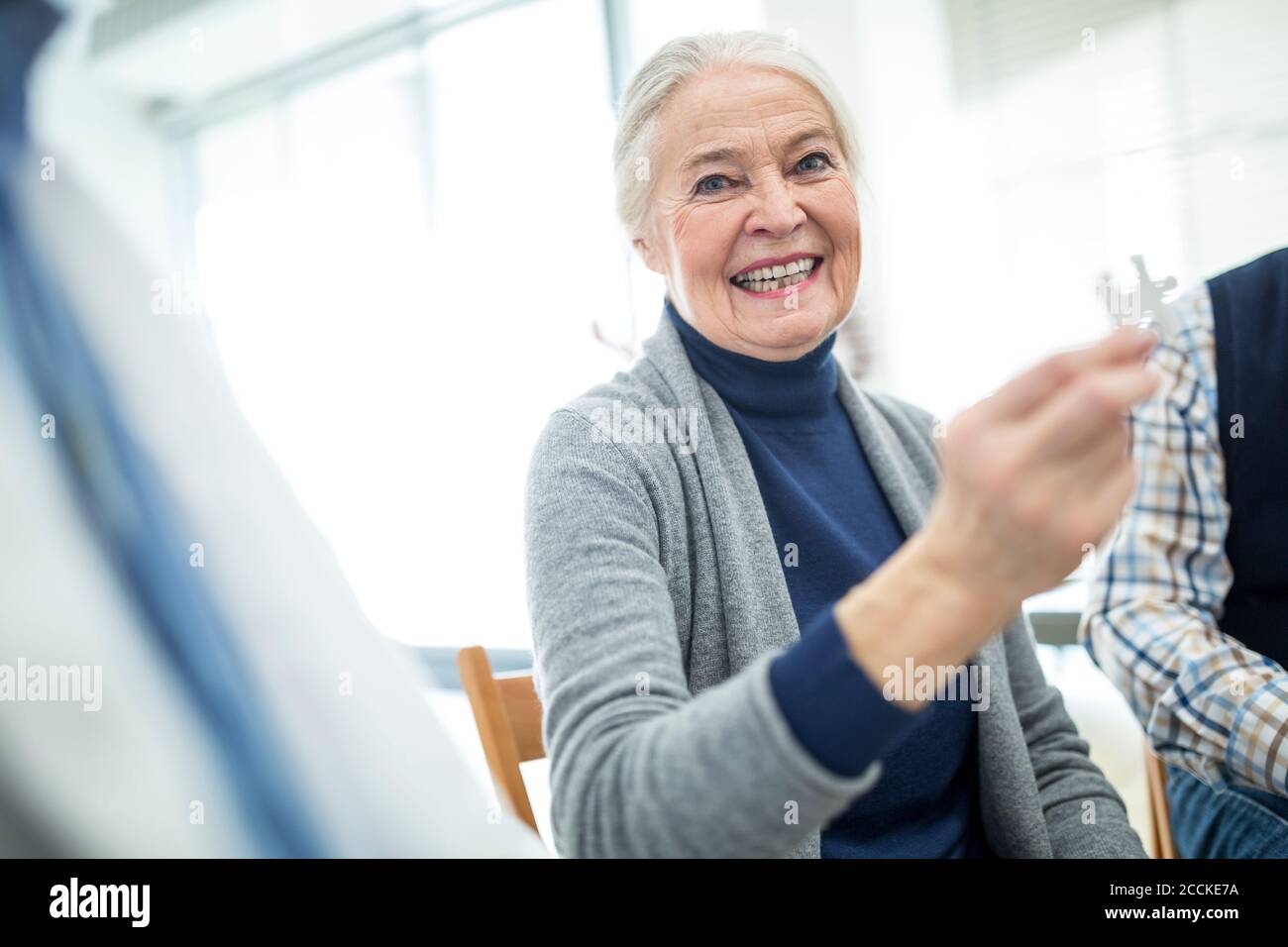 Laughing senior woman holding jigsaw piece in retirement home Stock Photo