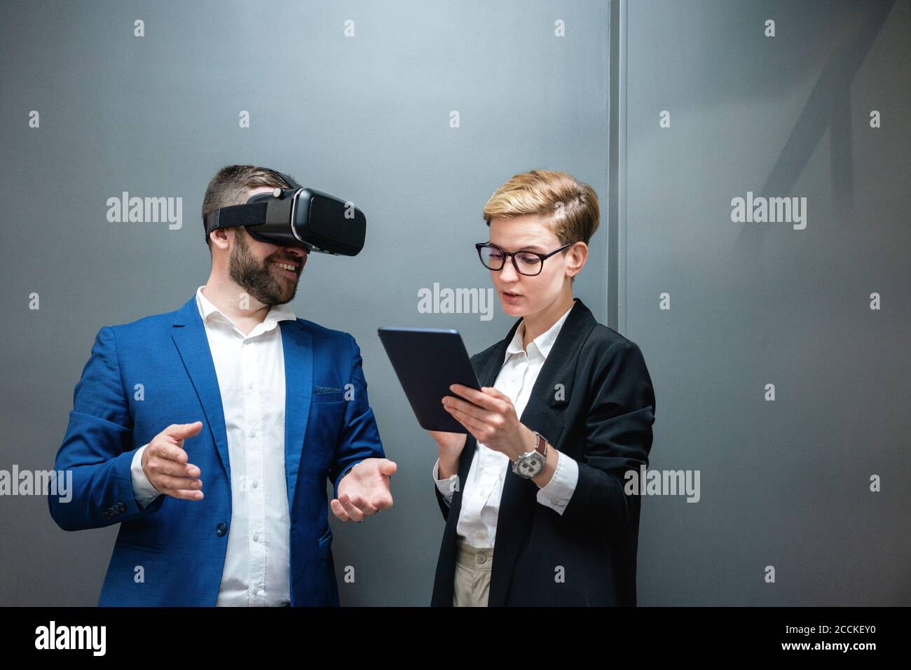 Female entrepreneur using digital tablet while analyzing colleague experiencing virtual reality simulation at office Stock Photo
