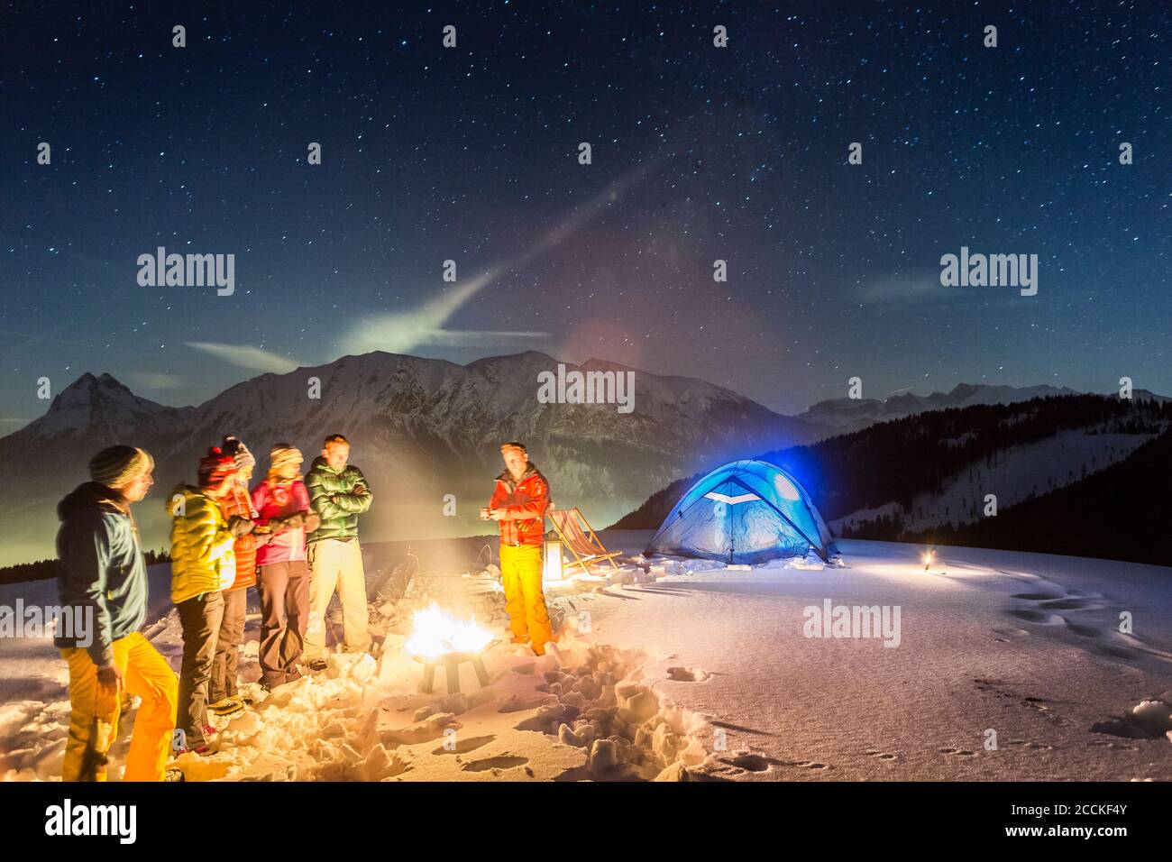 Nightscape of glowing tent in the snow and people around fire, Achenkirch, Austria Stock Photo