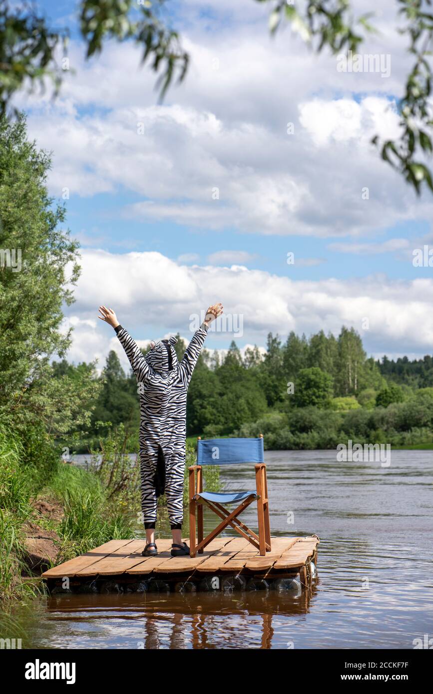 Boy in zebra costume with hands raised standing by lake Stock Photo
