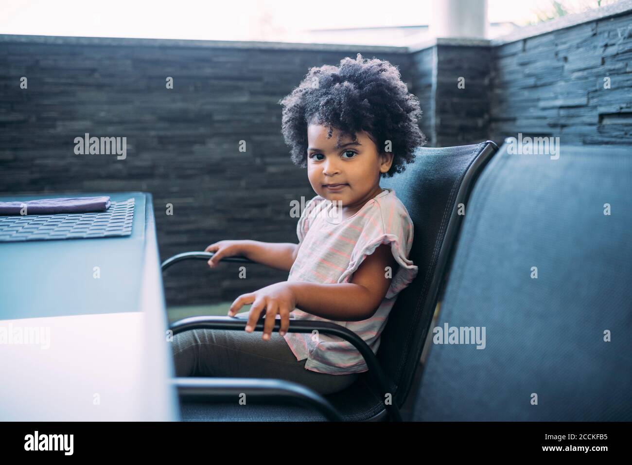Cute baby girl with curly hair sitting on chair at home Stock Photo