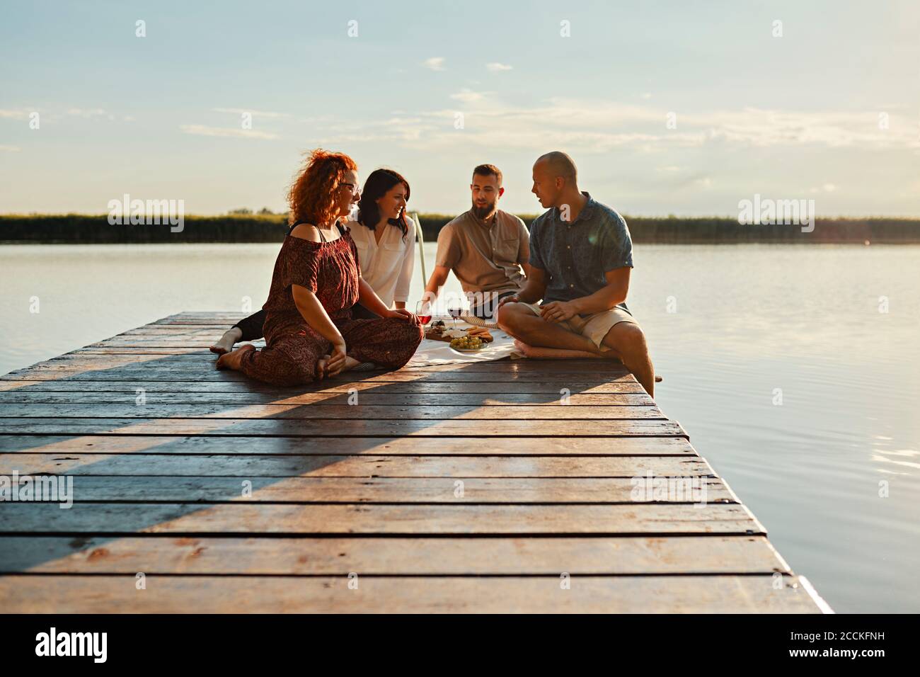 Friends having picnic on jetty at a lake at sunset Stock Photo