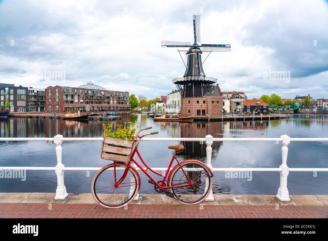 Netherlands, North Holland, Haarlem, Bicycle parked along railing of canal bridge with De Adriaan windmill in background Stock Photo