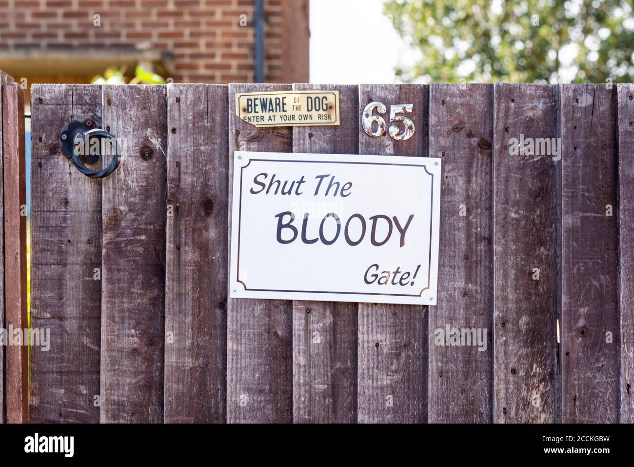 House garden gate with shut the bloody gate sign. Forceful message on garden gate. Offensive word, expletive, used with impact to get message across Stock Photo