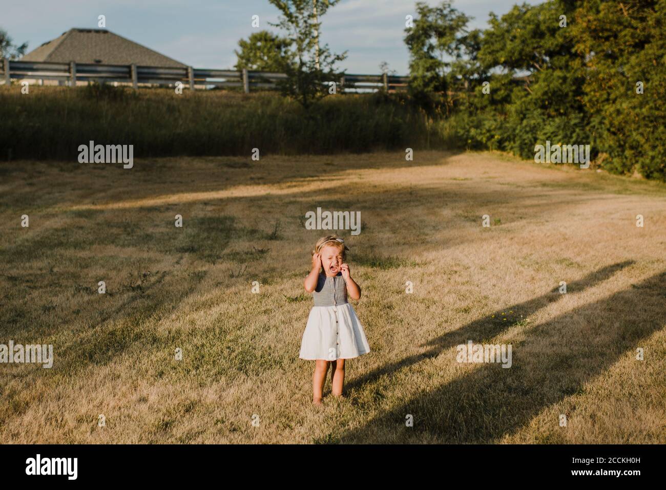 Crying little girl standing alone on a meadow Stock Photo