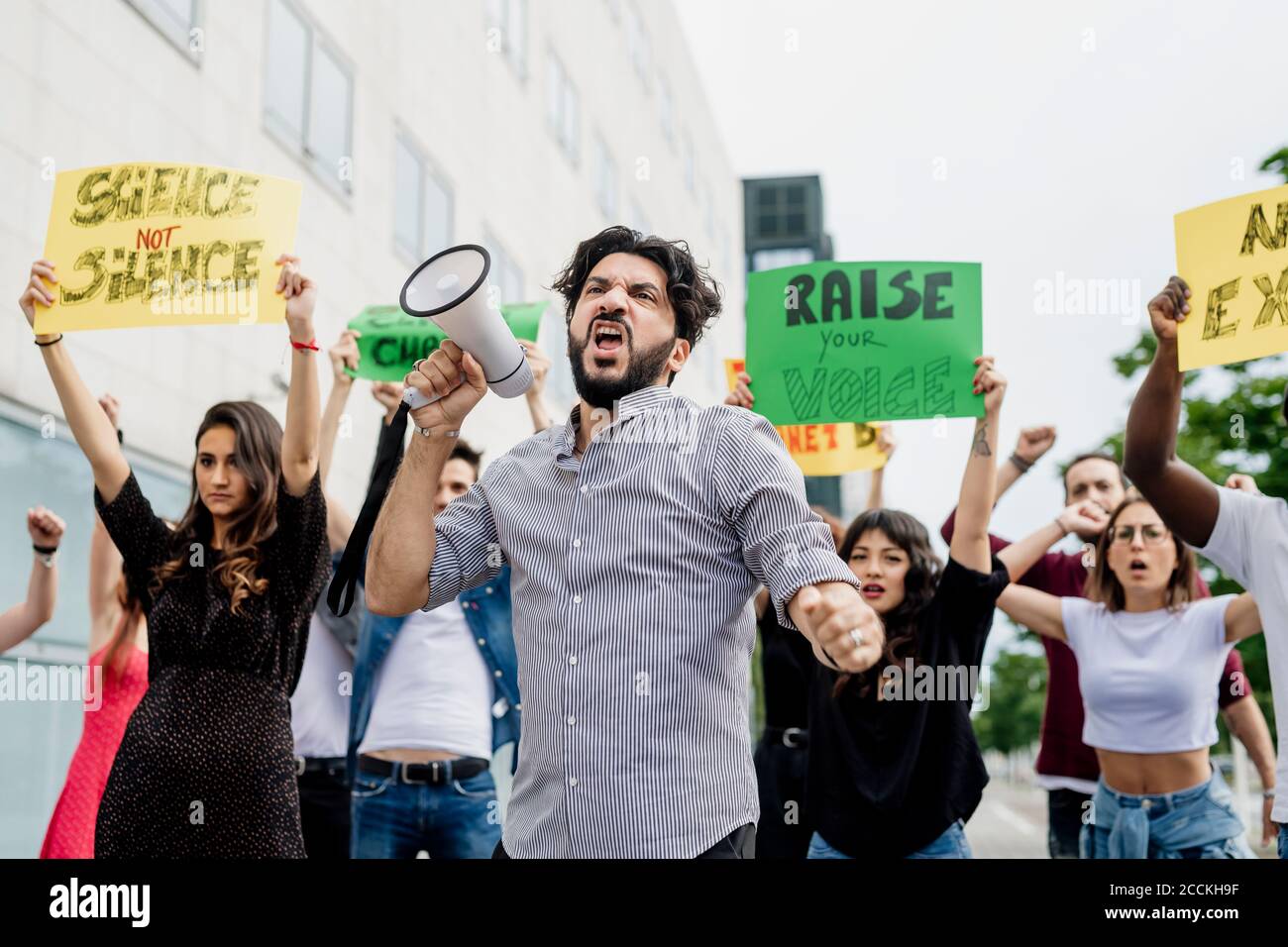 Man screaming through megaphone while protesting with people on street in city Stock Photo