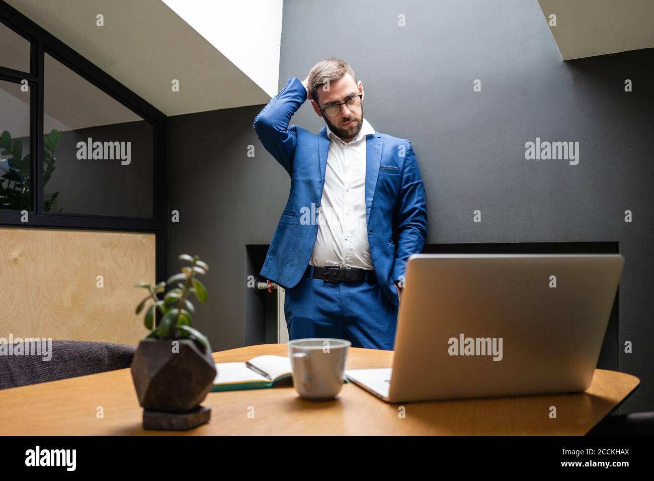 Confused businessman scratching head while looking at laptop on desk in creative office Stock Photo