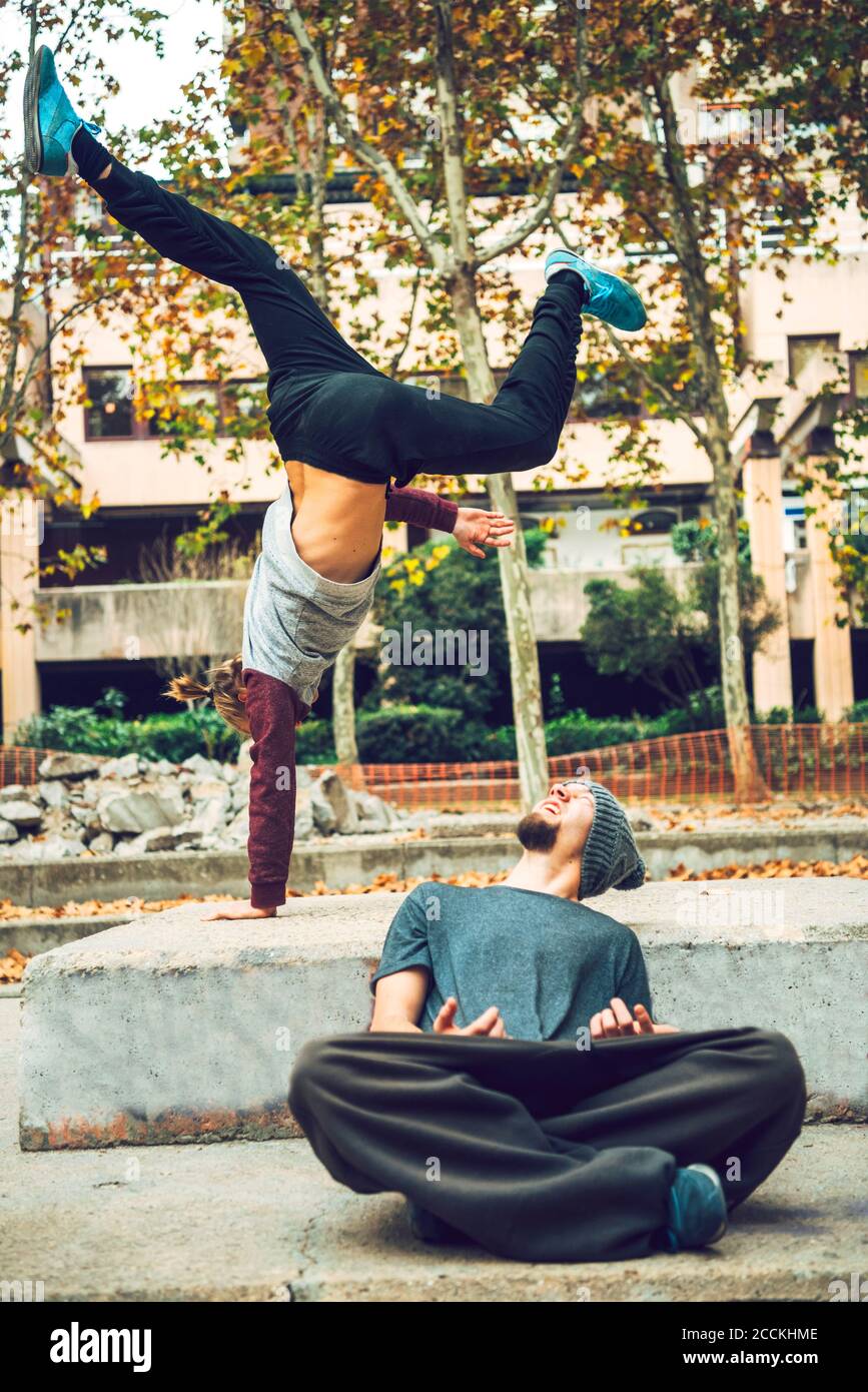 Young man looking at friend performing handstand in public park Stock Photo