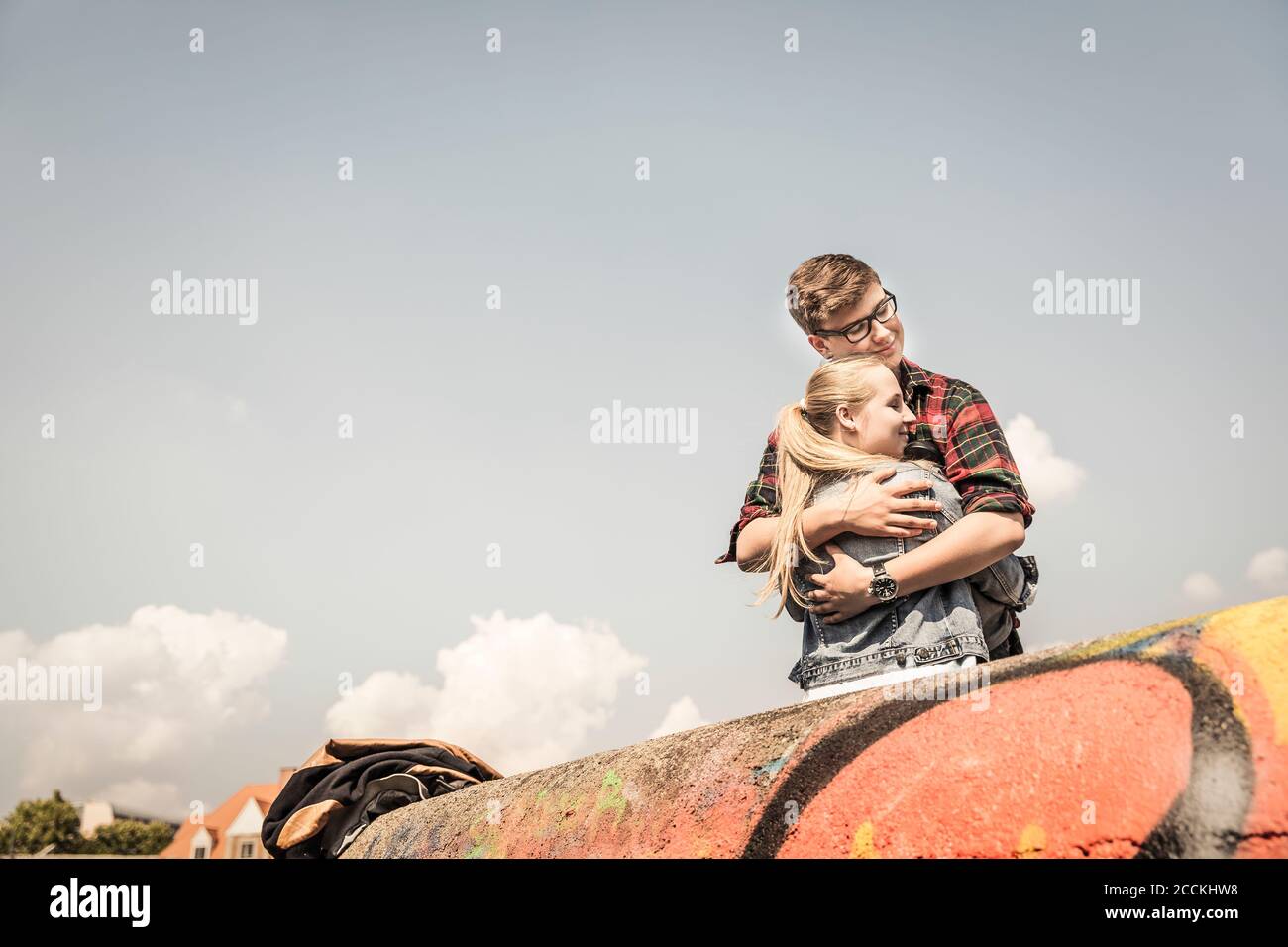 Teenage couple hugging behind a graffiti wall Stock Photo