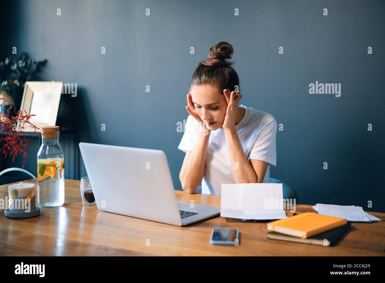 Female entrepreneur with head in hands sitting at desk against wall