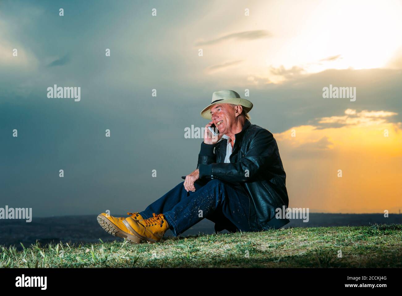 Smiling senior man talking on mobile phone against cloudy sky during sunset Stock Photo