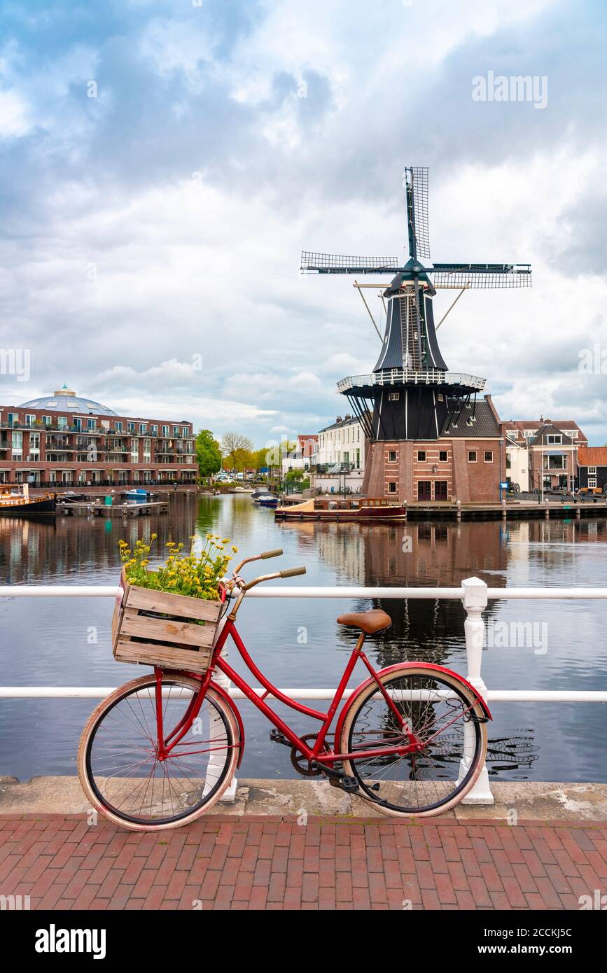 Netherlands, North Holland, Haarlem, Bicycle parked along railing of canal bridge with De Adriaan windmill in background Stock Photo