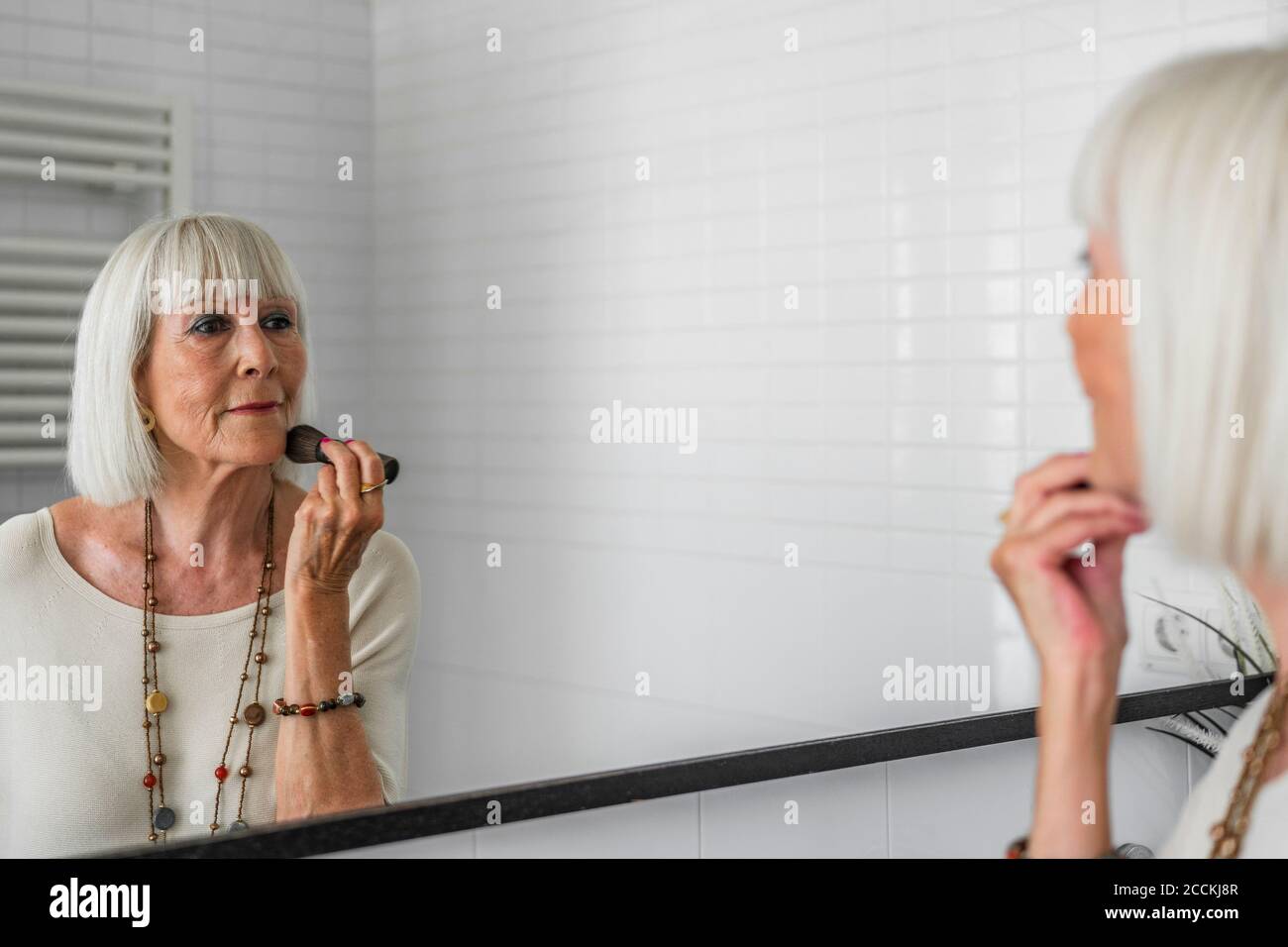 Senior woman applying make-up while looking in mirror at home Stock Photo