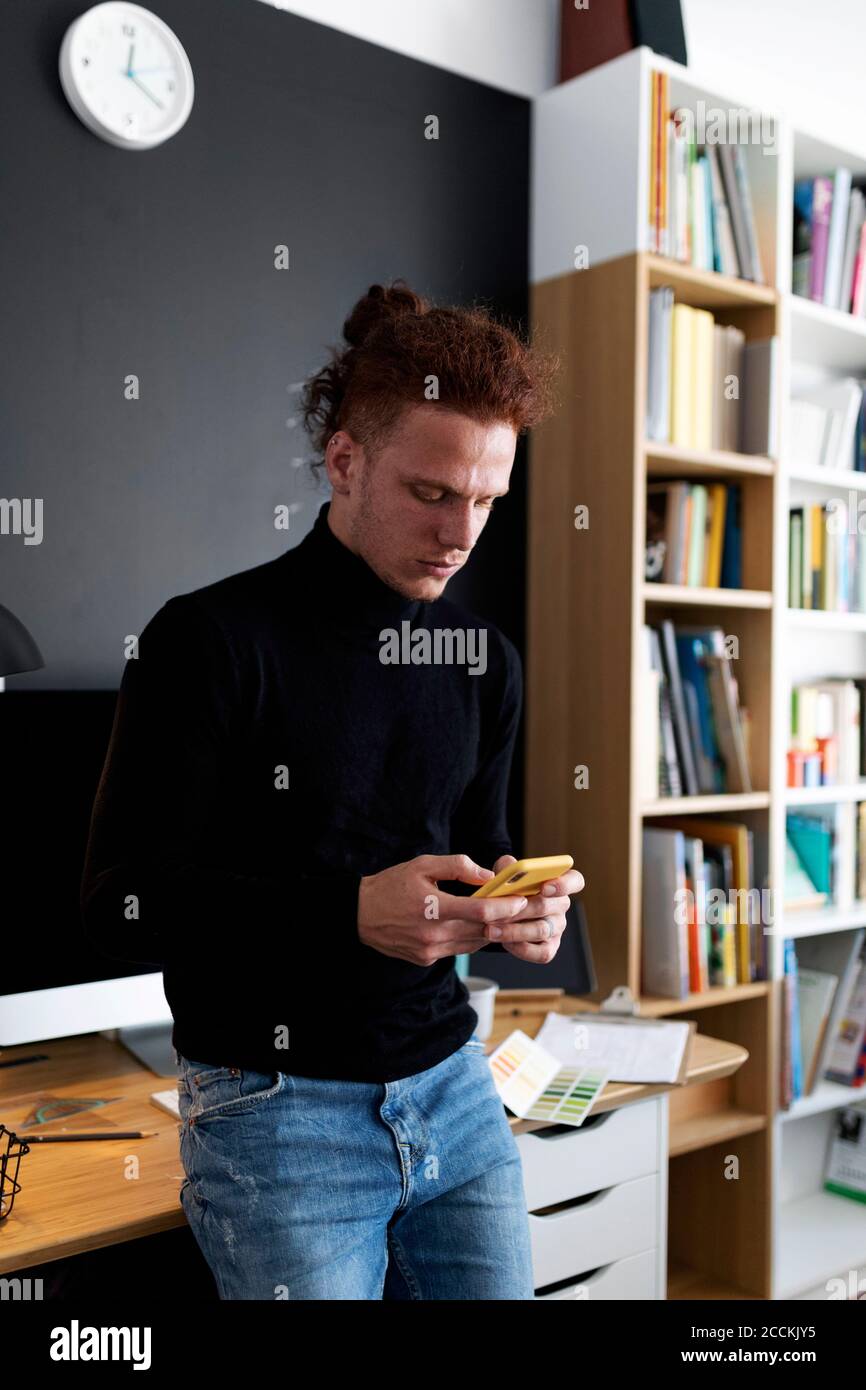 Young man using smart phone while standing at home office Stock Photo