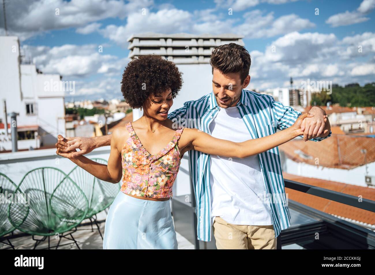 Multi-ethnic couple dancing on penthouse patio during sunny day Stock Photo