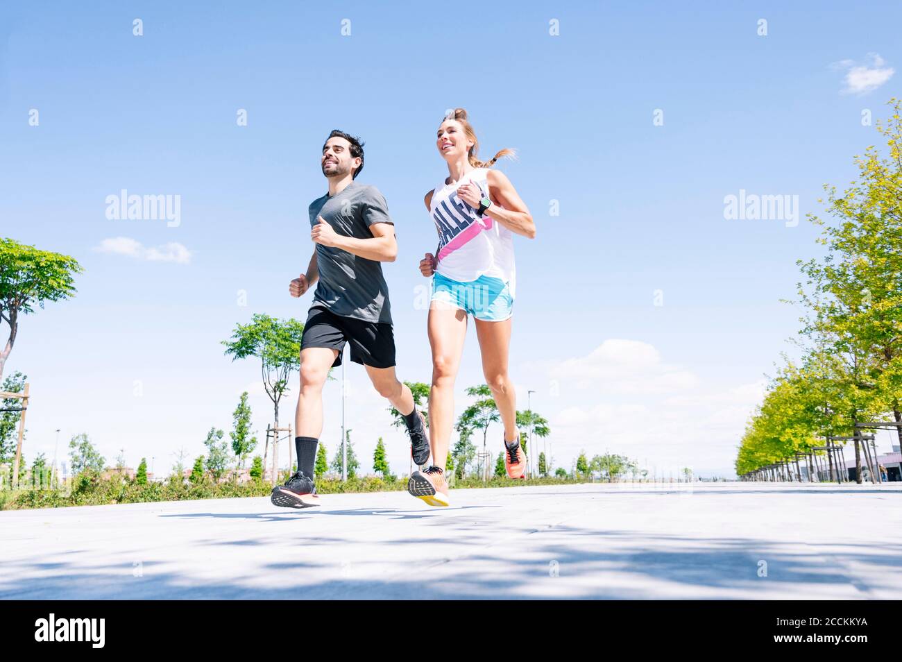 Mid adult couple running on road against blue sky during sunny day Stock Photo