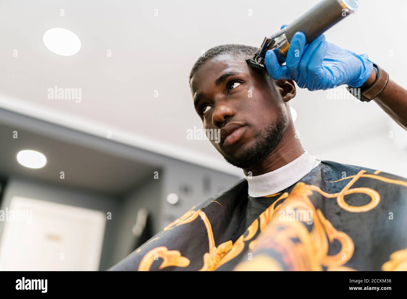 Male hairdresser wearing glove cutting young man's hair with razor in