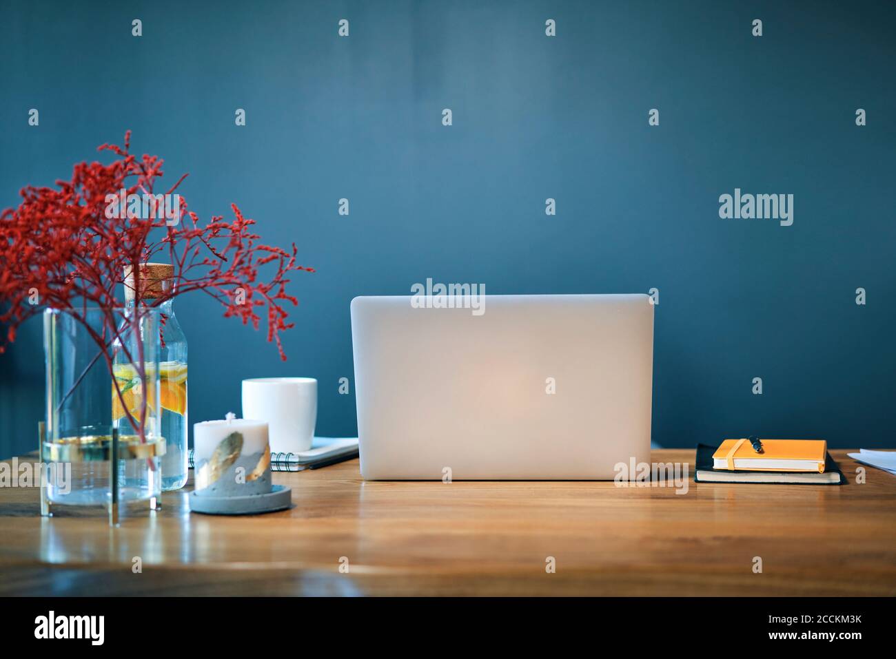 Laptop with diaries and decorations on desk against blue wall in home office Stock Photo