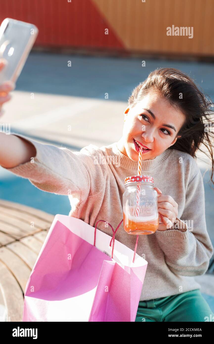Young woman taking selfie while sipping juice at shopping mall Stock Photo
