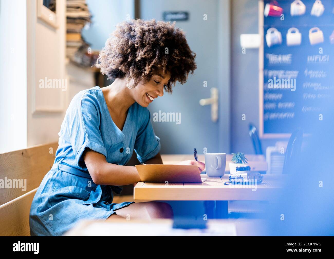 Happy woman writing in book while sitting at table in coffee shop Stock Photo