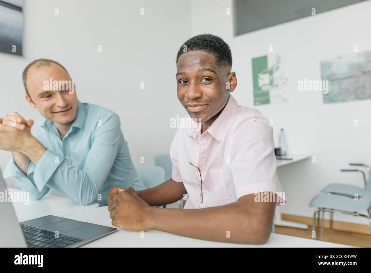 Smiling coworkers working on laptop while sitting at workplace Stock Photo