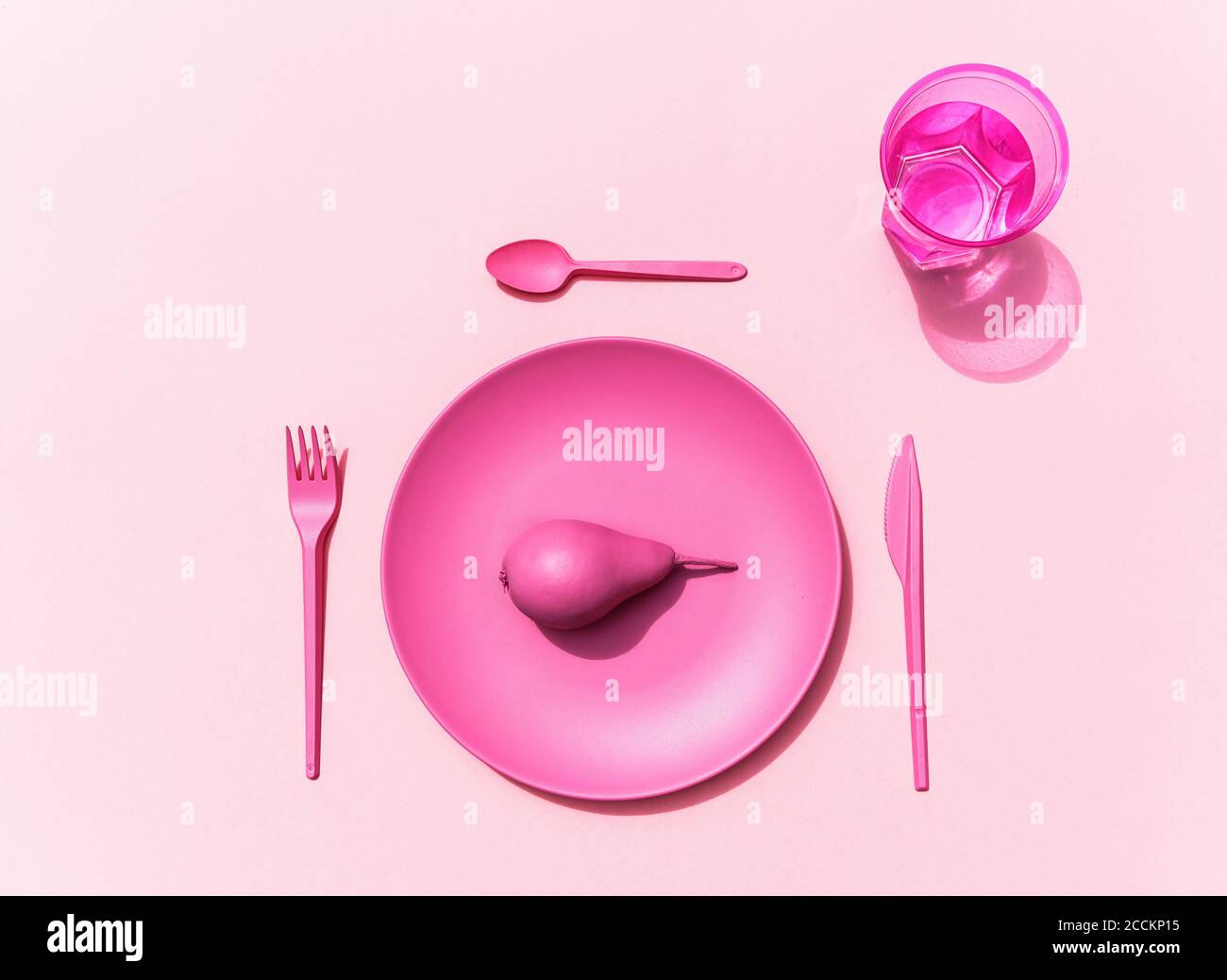 Studio shot of pink plastic plate, plastic cutlery, glass of water and pink pear Stock Photo