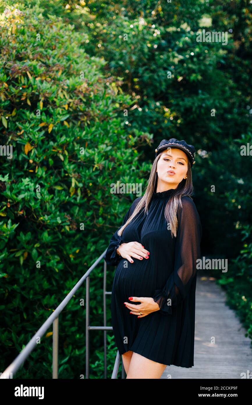 Pregnant woman puckering while standing on footbridge against trees in park Stock Photo