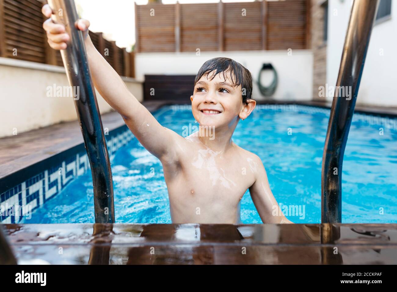 Smiling boy holding ladder in swimming pool Stock Photo