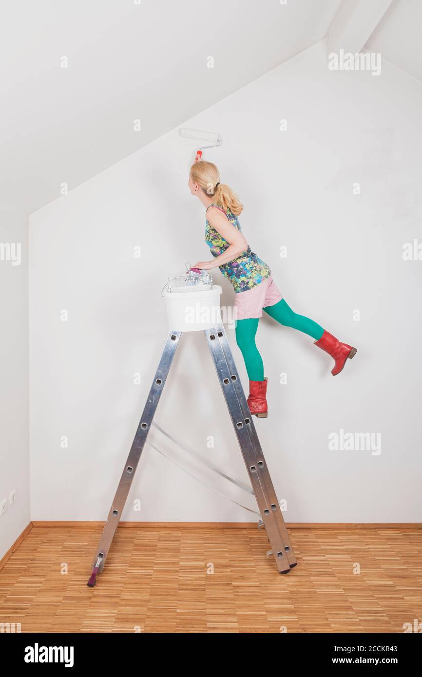 Mature woman painting wall while standing on step ladder at home Stock