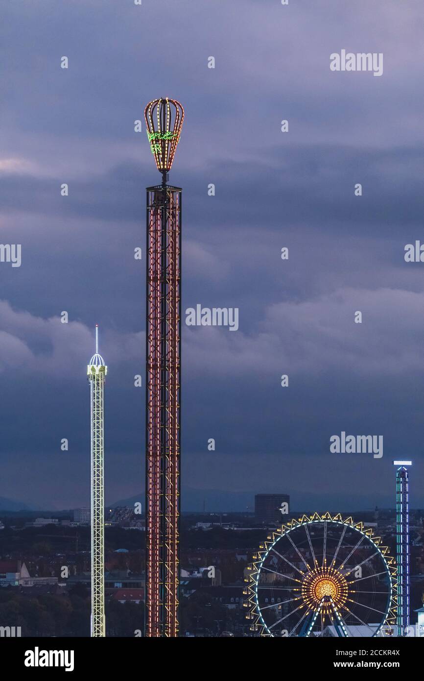 Germany, Bavaria, Munich, Aerial view of illuminated free fall and chain swing towers at dusk Stock Photo