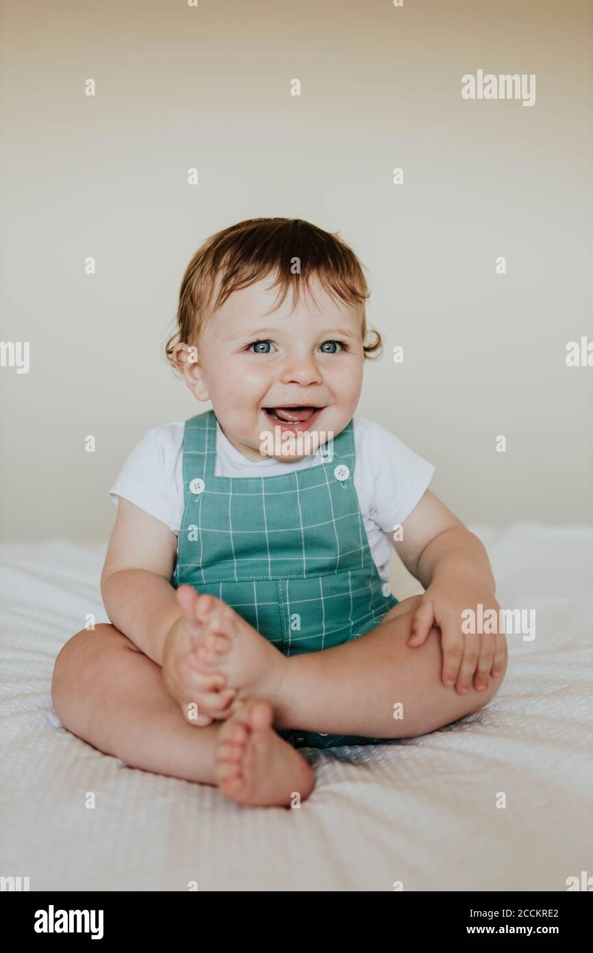 Closeup of cute baby girl laughing while sitting on bed against wall at home Stock Photo Alamy