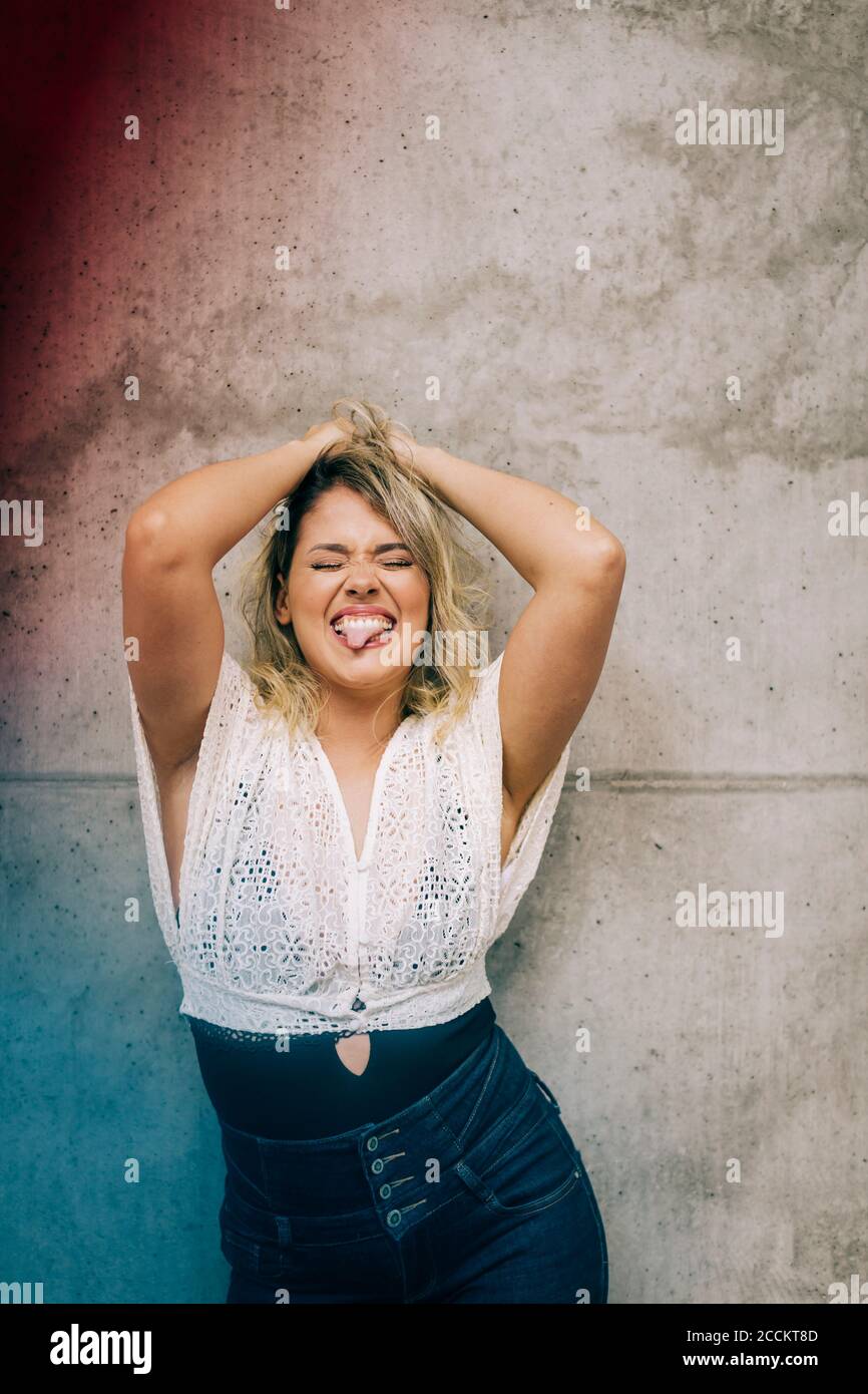 Young woman standing with hands in hair against wall Stock Photo - Alamy
