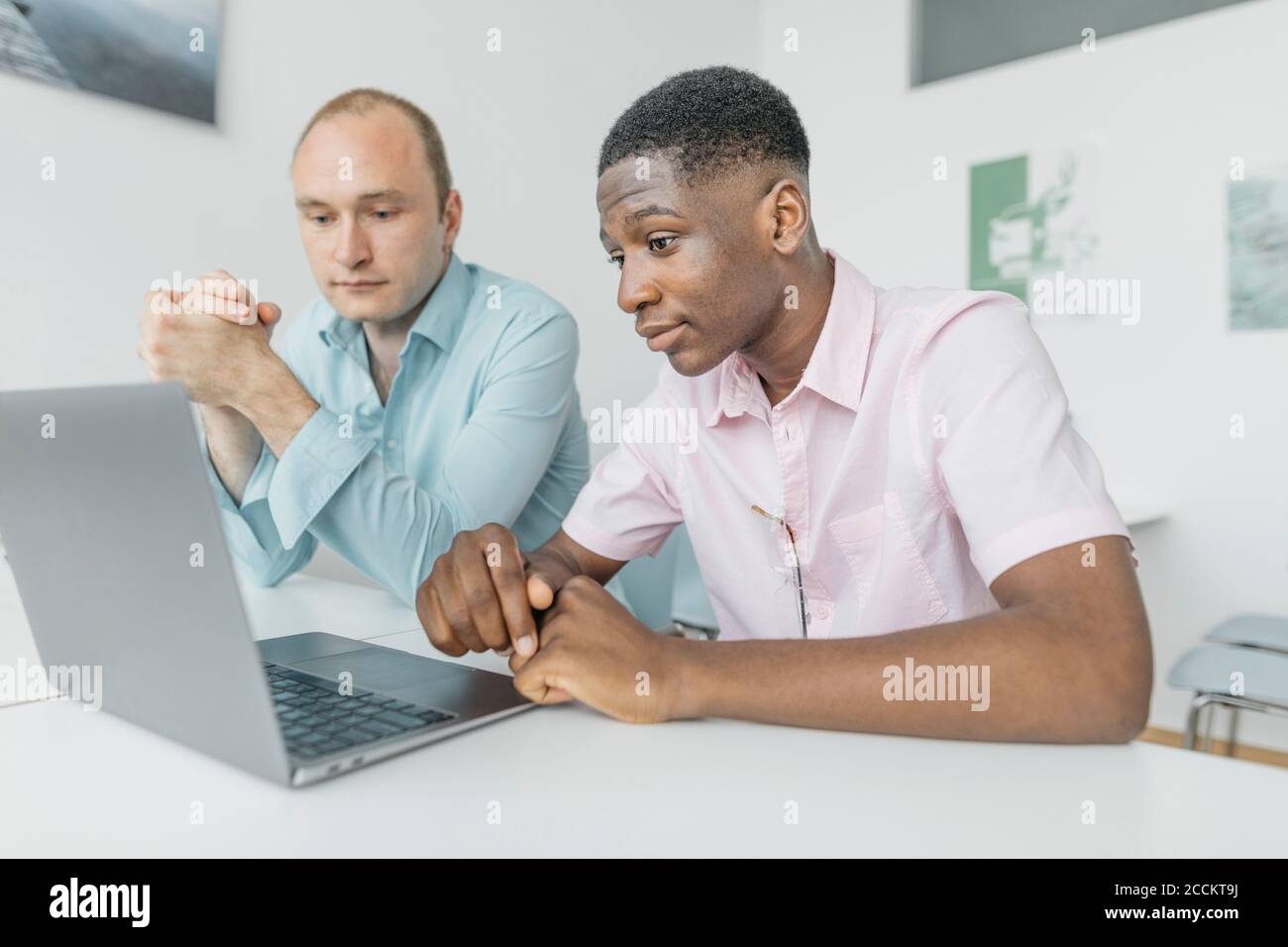 Coworkers working on laptop while sitting at workplace Stock Photo