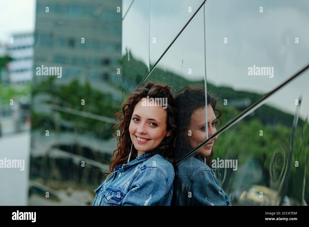 Smiling young woman leaning on mirror wall Stock Photo