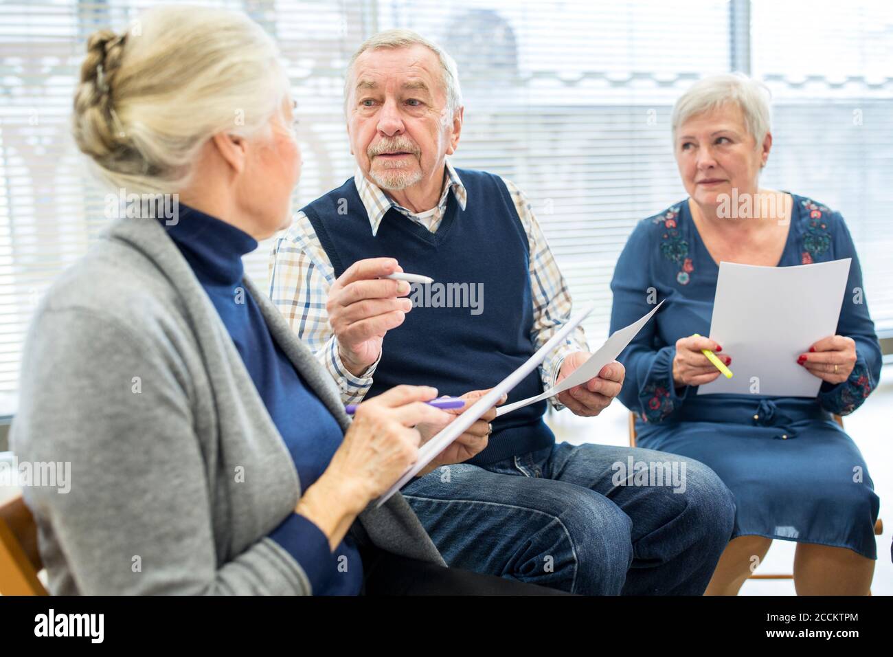 Seniors in therapy group in retirement home writing down notes on sheets of paper Stock Photo