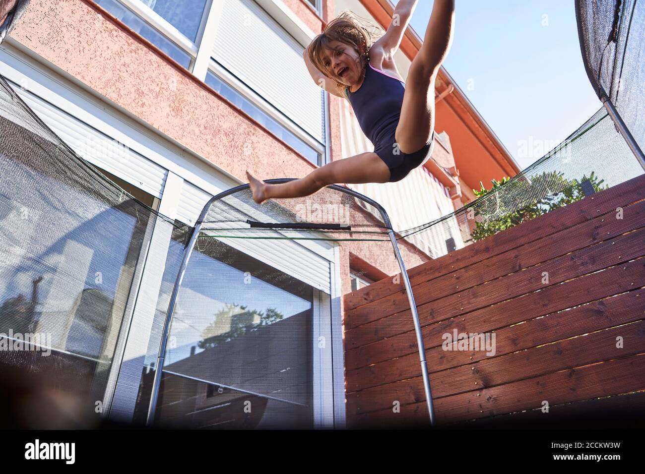 Playful girl jumping on trampoline against house during sunny day Stock Photo