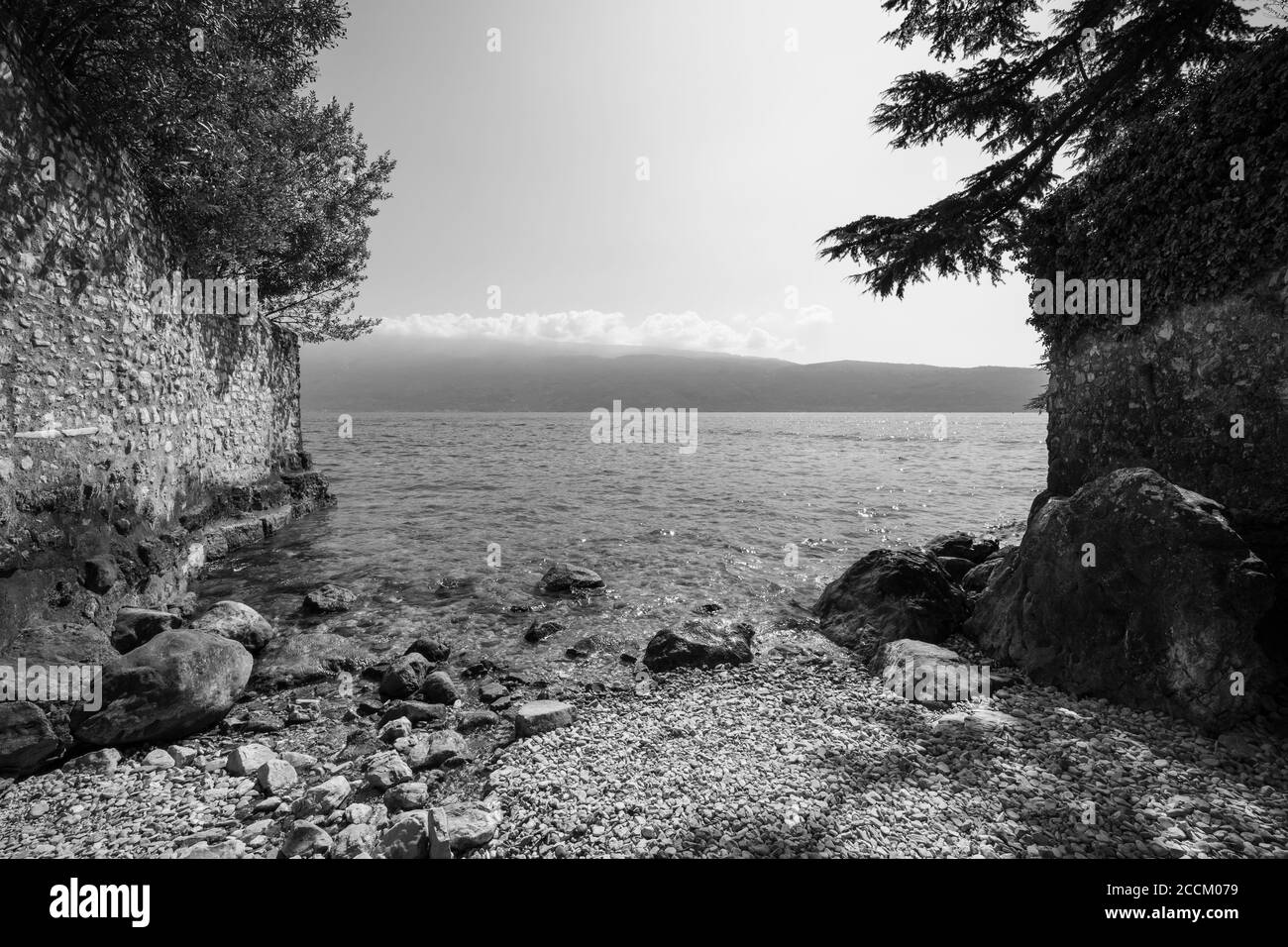 Tiny beach on Lake Garda in Gargnano, Brescia, Italy, panoramic view from the western shore towards the Verona side, Black and White photo Stock Photo