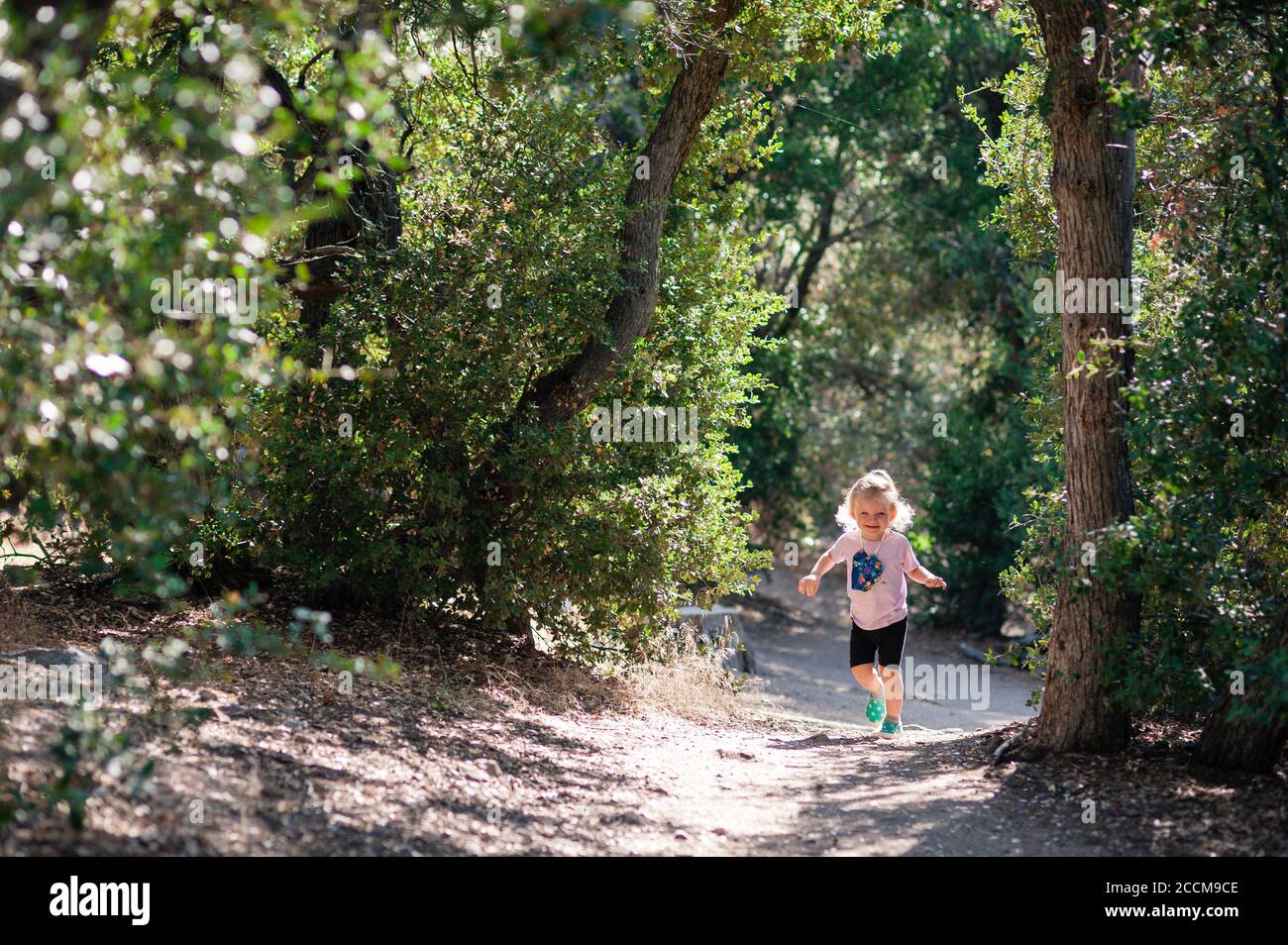 Happy 2 yo little girl doing her first hike through the forest at the Woodland Trail in Big Bear, California. Stock Photo