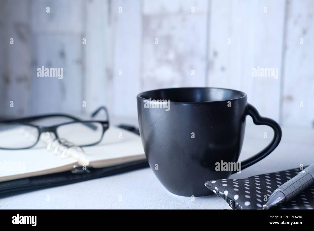 black mug mockup, modern workspace with notepad and eyeglass on table. Stock Photo