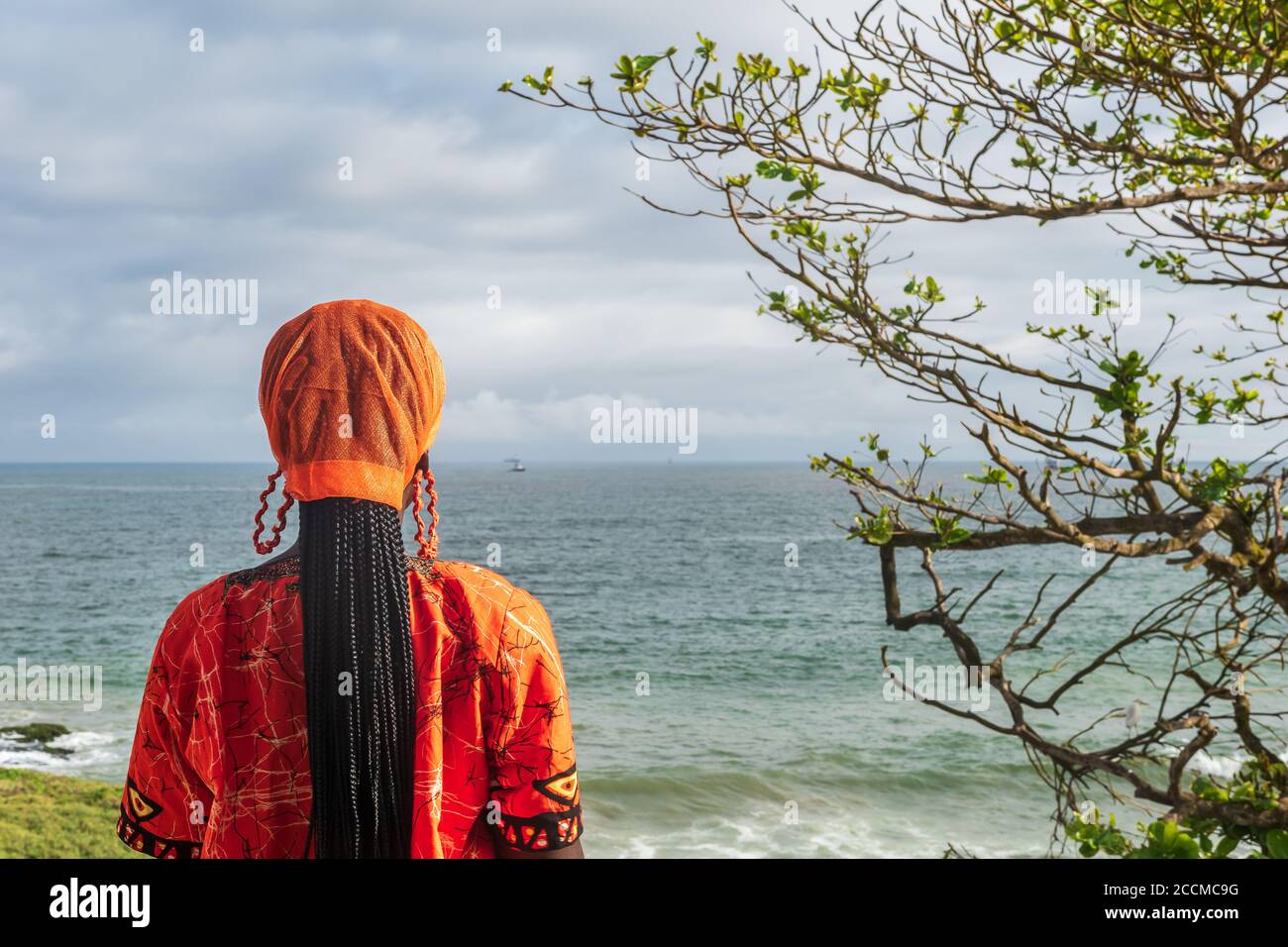 African Woman wearing orange traditional dress from Ghana looks over the horizon in Takoradi Ghana West Africa Stock Photo