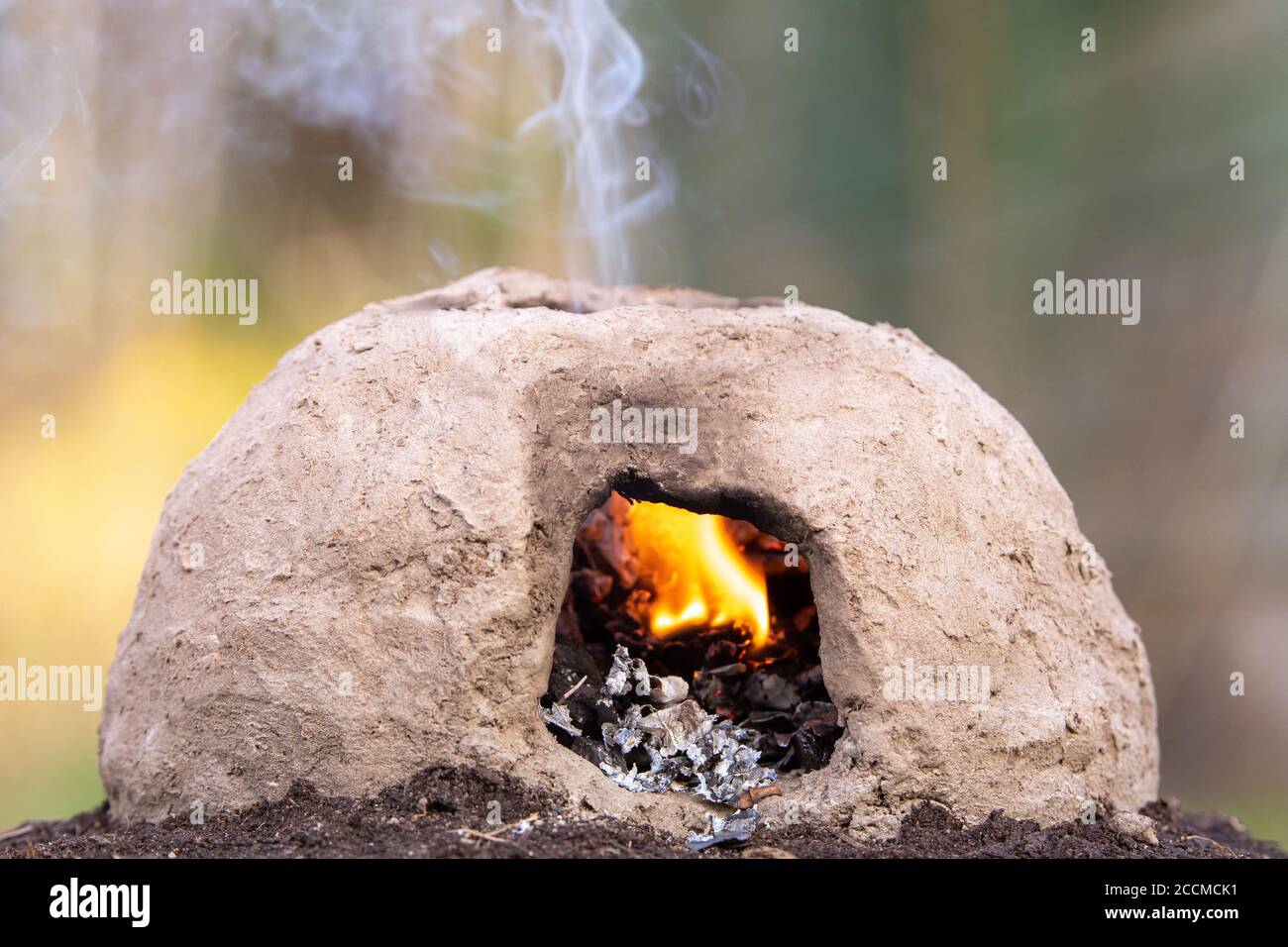 A small, primitive oven made from mud. A fire burns inside and smoke rises from a hole in the top. Stock Photo